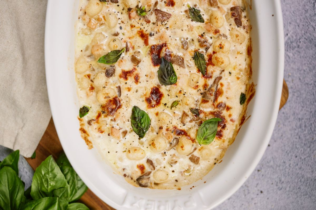 creamy gnocchi casserole in white baking dish topped with fresh basil