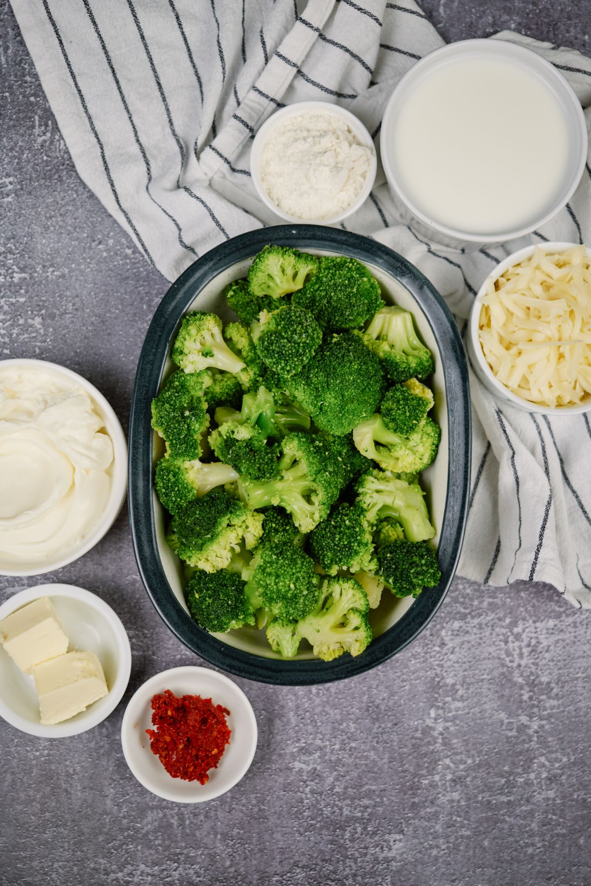 large bowl of fresh broccoli next to small white bowls of butter and cheese on gray table