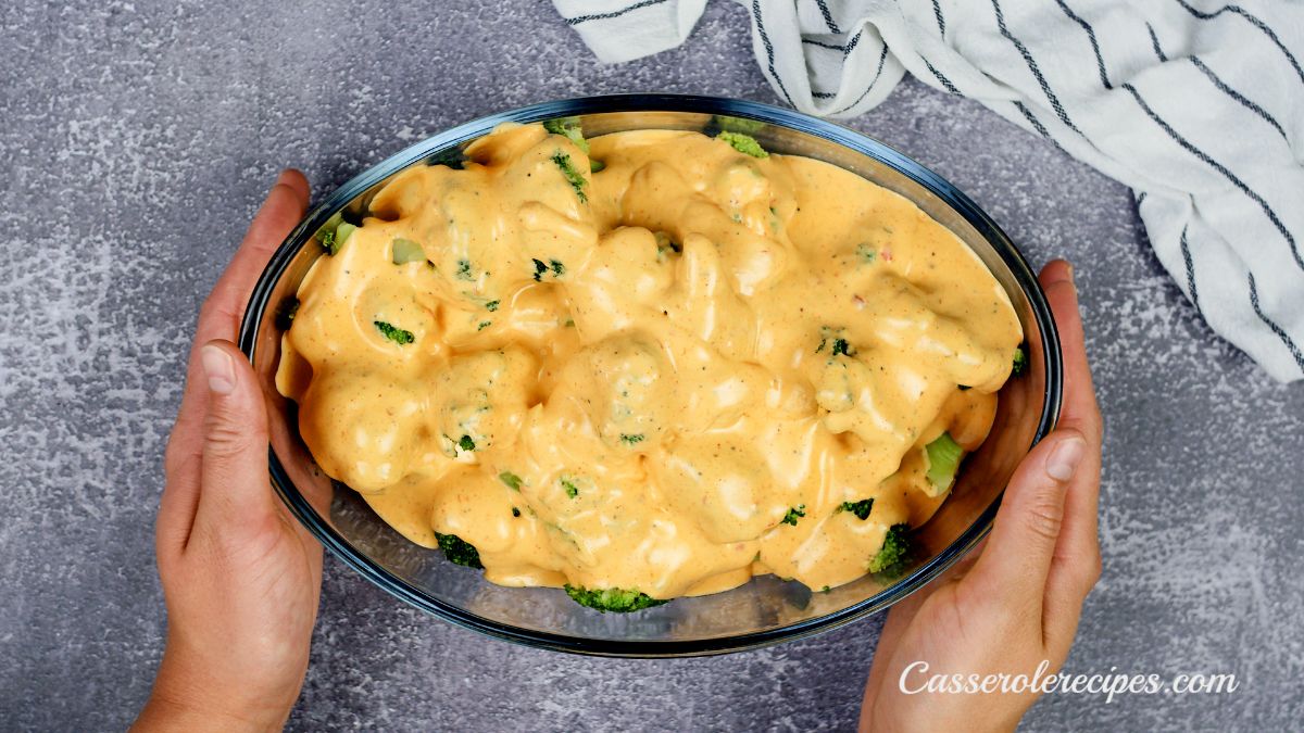 hands holding casserole dish of broccoli and cheese above gray table