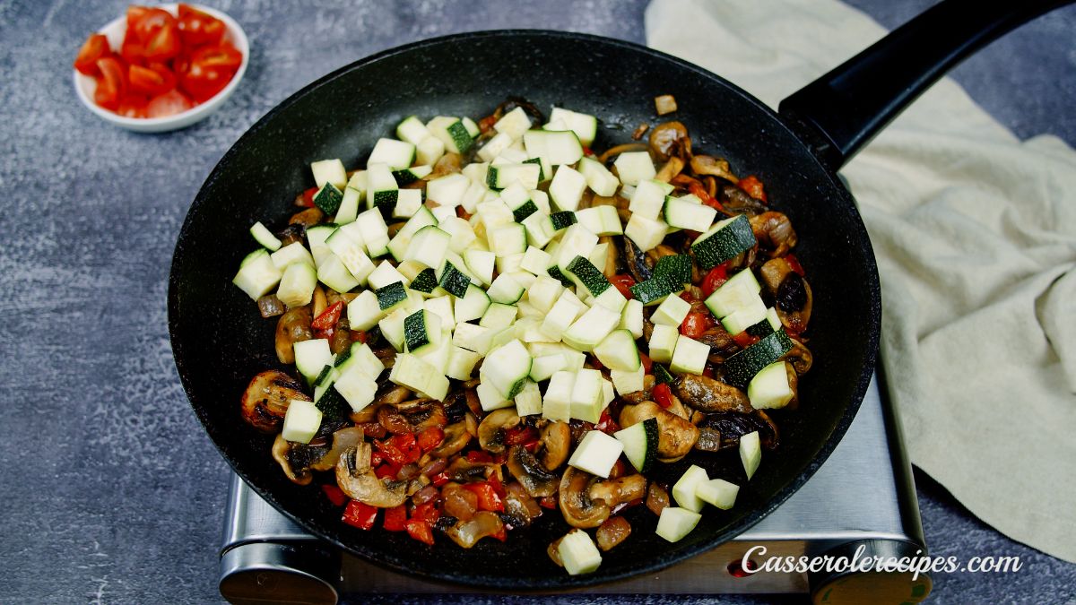 zucchini on top of peppers and mushrooms in black skillet on hot plate