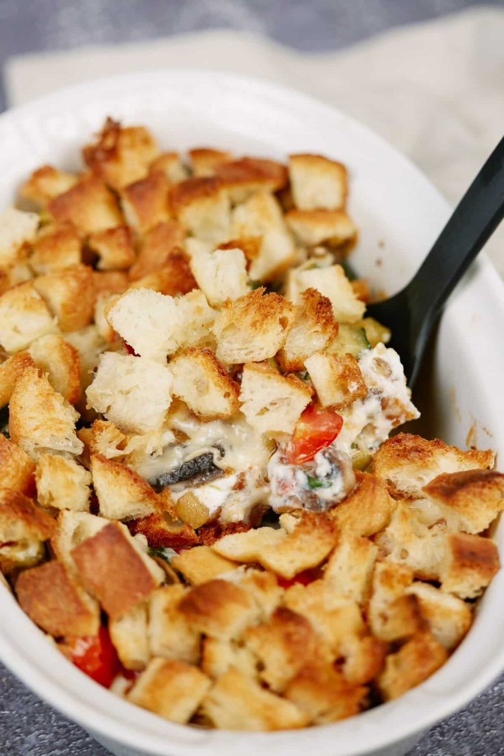 white oval baking dish of casserole topped with croutons and black spoon in casserole