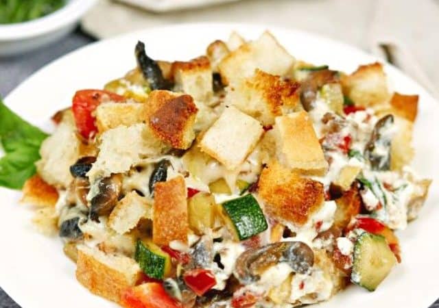 round white bowl of zucchini casserole topped with croutons sitting on table with white napkin in background