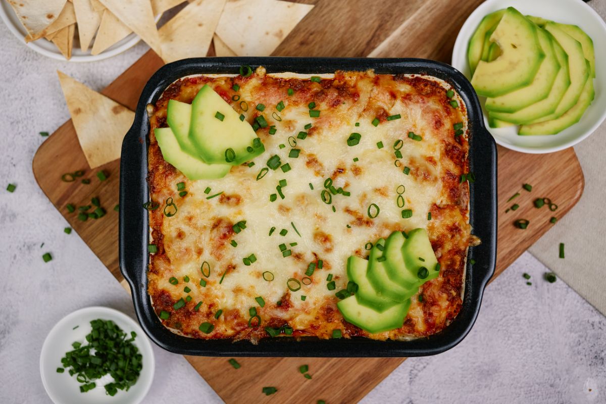 casserole dish of keto taco casserole topped with avocado slices on top of cutting board