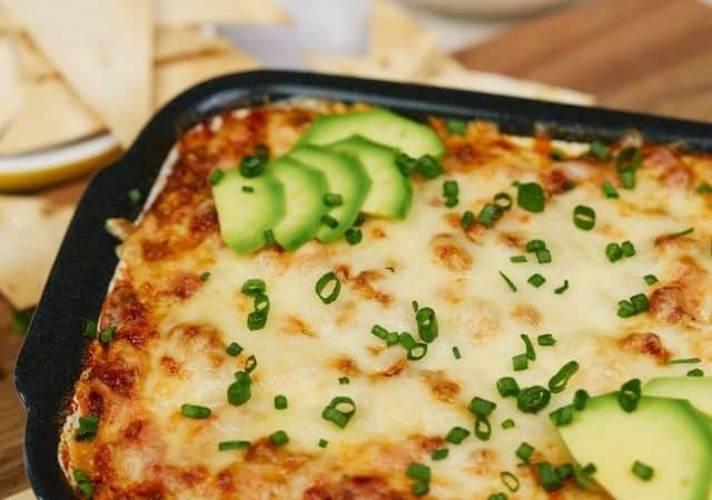 black trim baking dish with keto taco casserole sitting on cutting board by white bowl of avocado slices