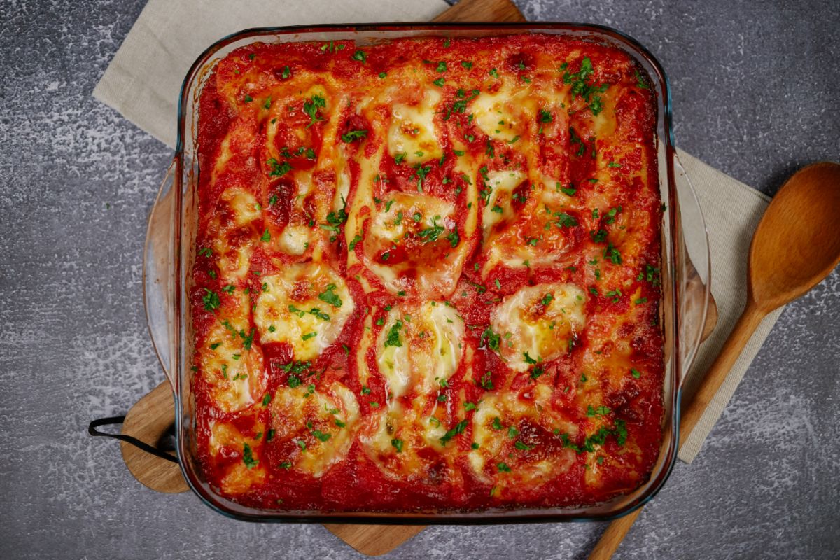 square casserole dish topped with cheese and red sauce on gray table
