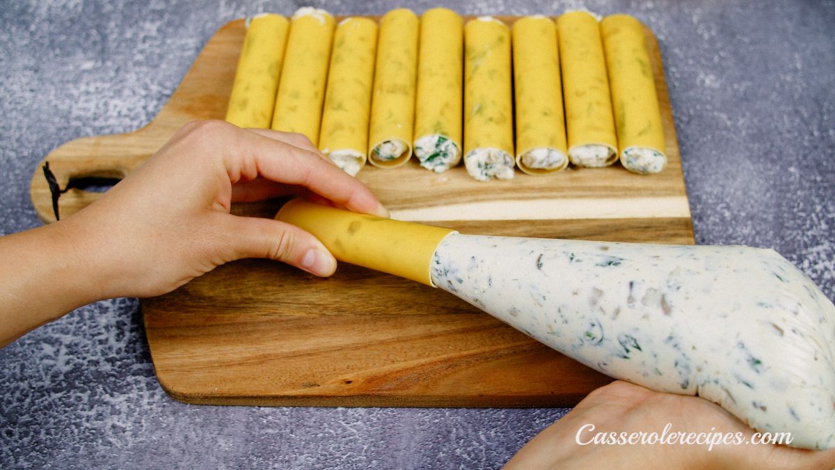 hand piping cheese into raw manicotti