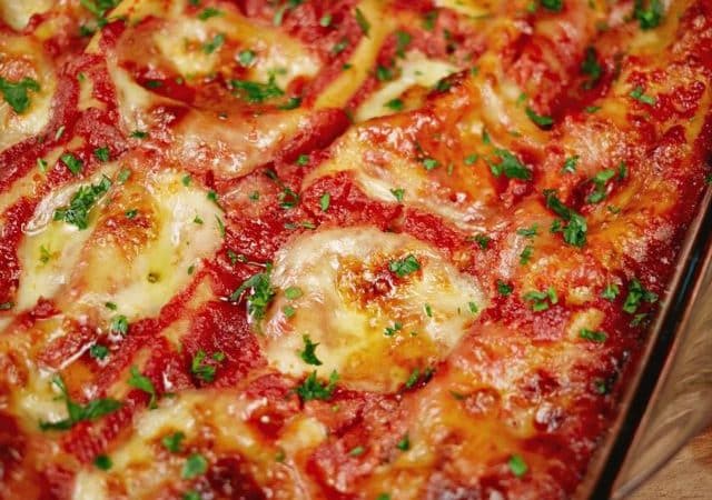 manicotti stuffed pasta in red sauce topped my mozzarella in glass baking dish