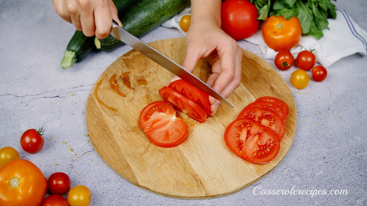 hand slicing tomato on round cutting board