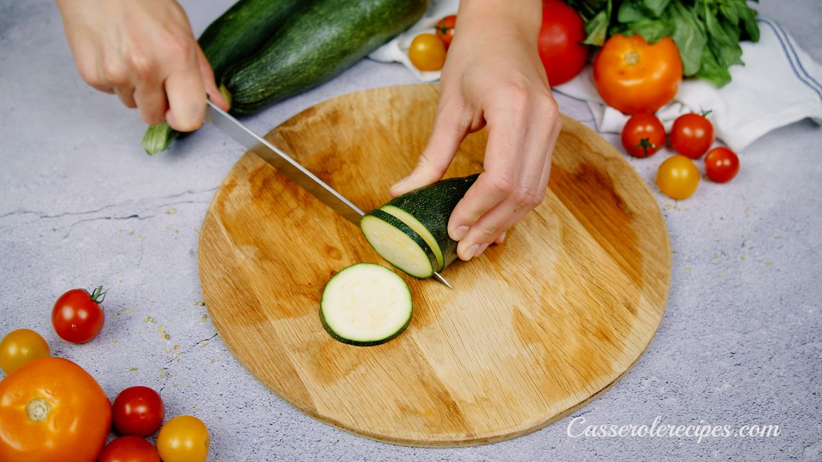 hand slicing zucchini on round cutting board