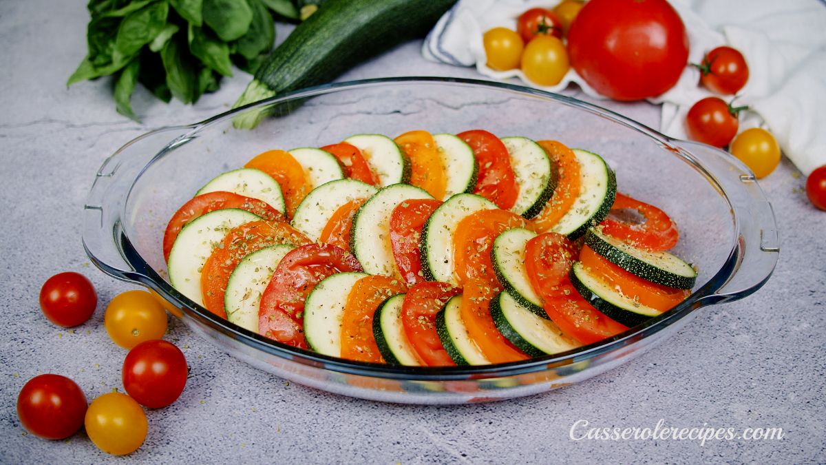 spices sprinkled over zucchini and sliced tomato in glass casserole dish