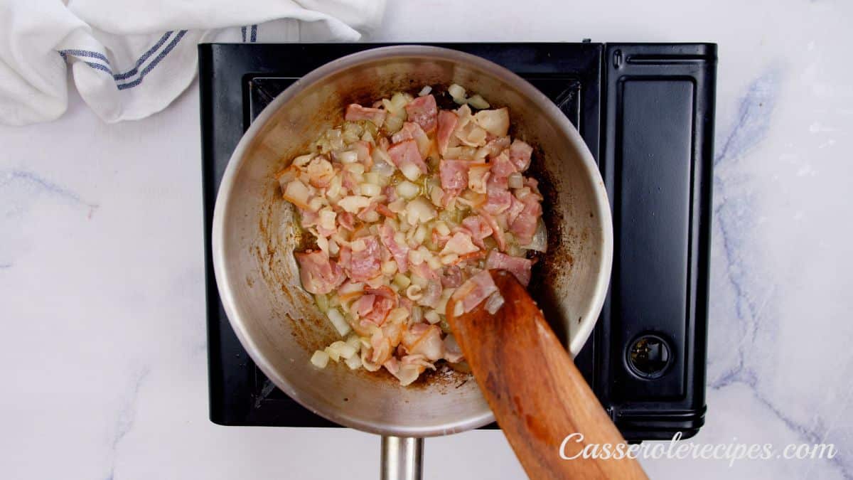 wooden spoon stirring onions and bacon in skillet