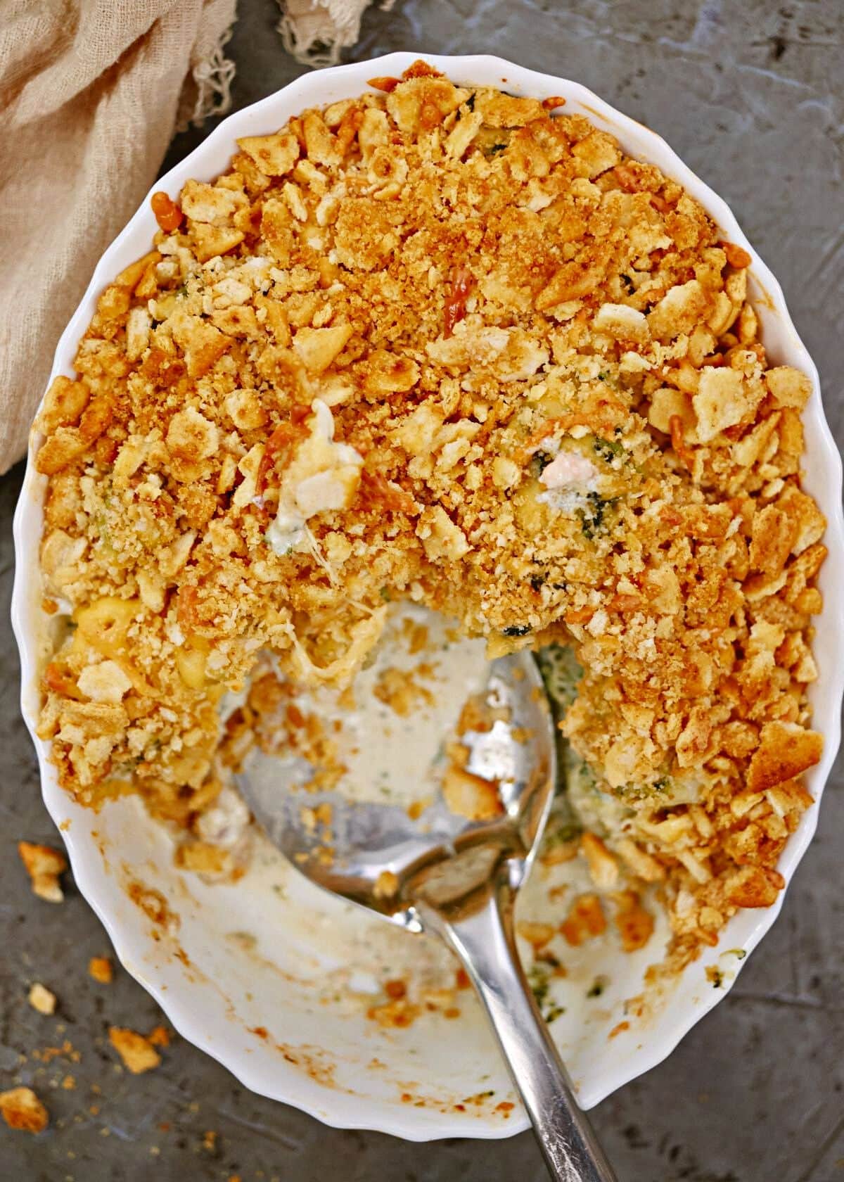 white oval baking sheet of broccoli cheese casserole with spoon in the dish