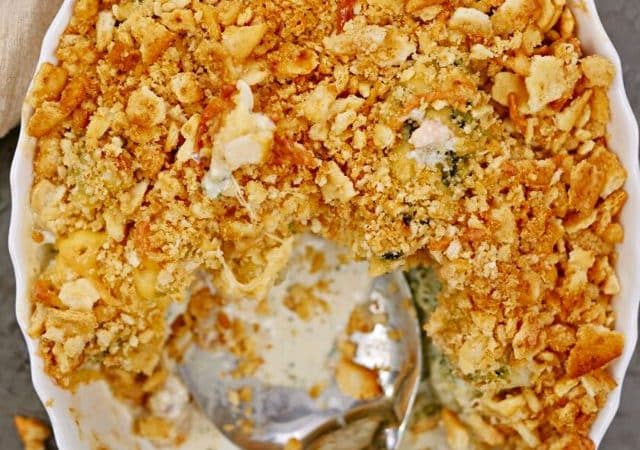 white oval baking sheet of broccoli cheese casserole with spoon in the dish