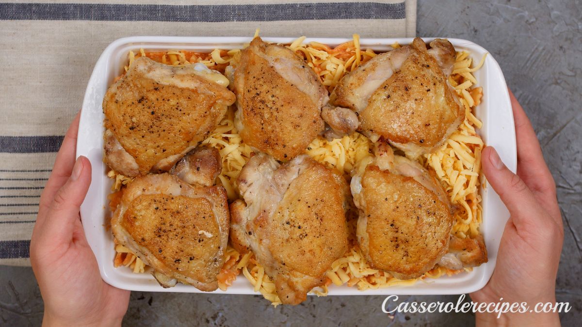 chicken thighs on top of pasta in white baking dish before baking