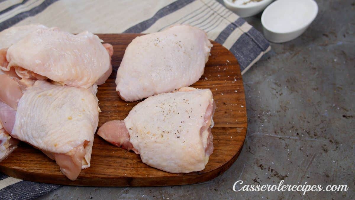 raw chicken thighs on cutting board being seasoned