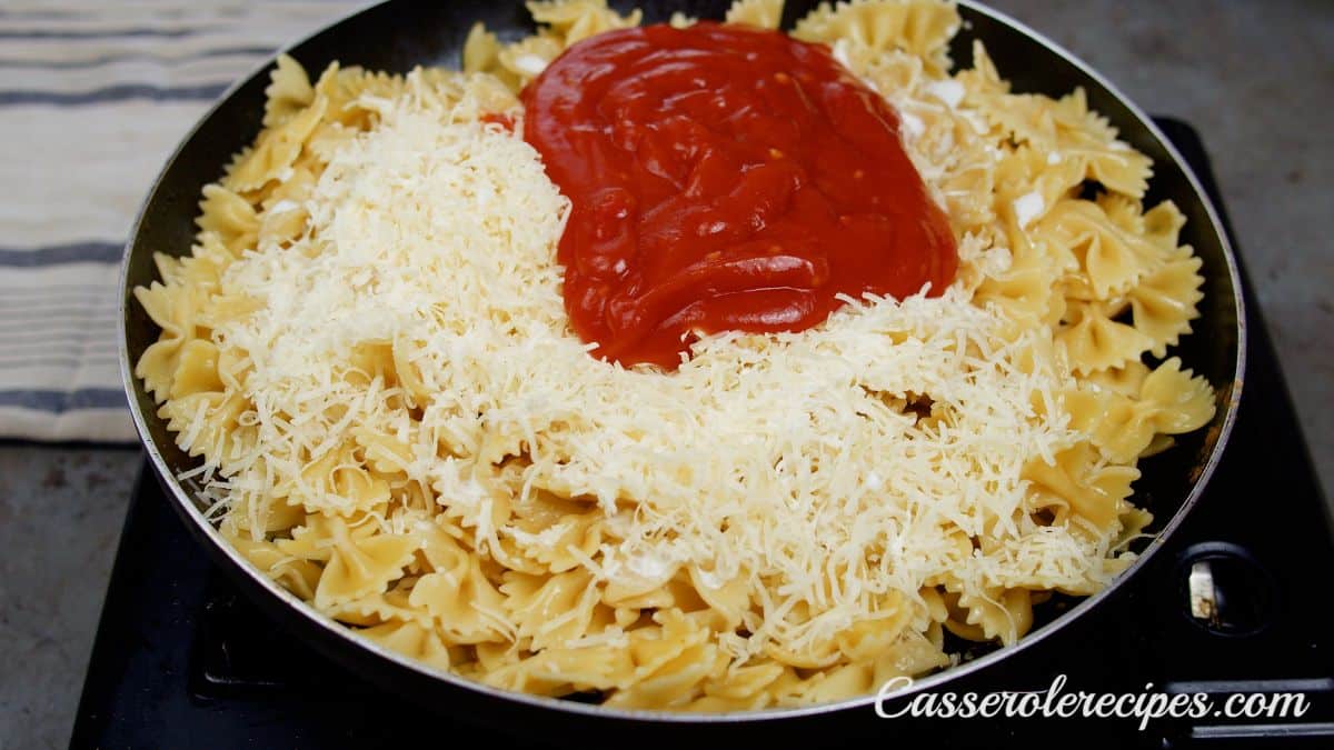 bowtie pasta in skillet with shredded cheese and tomato sauce