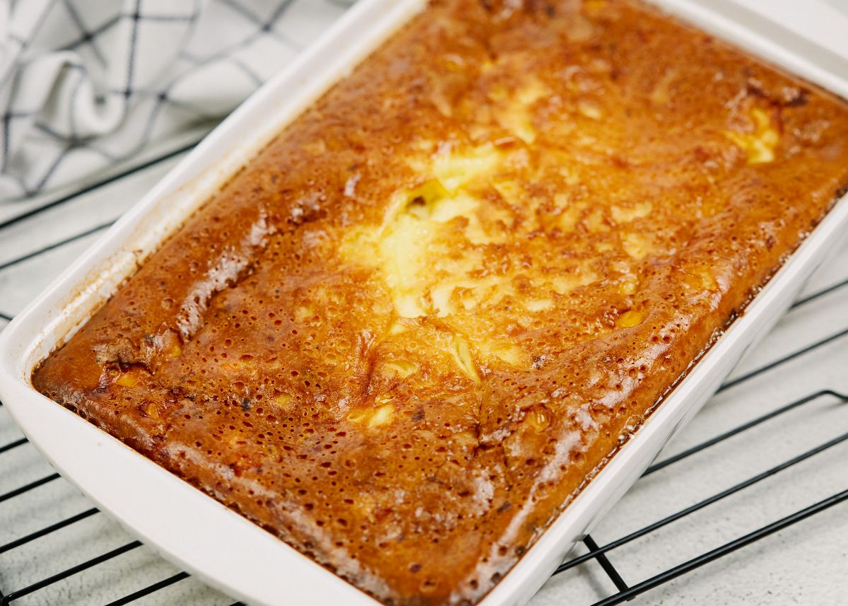 rectangular white baking dish of corn pudding casserole sitting on black wire rack over white table