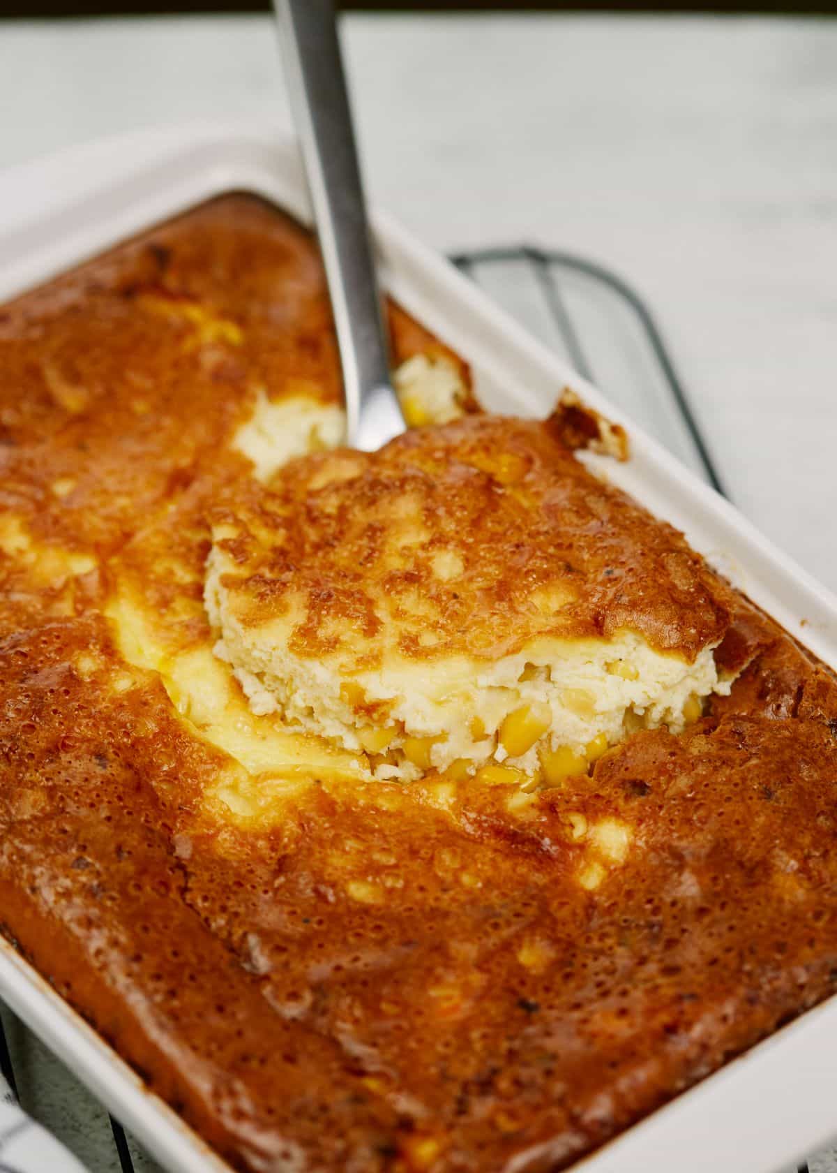 silver spoon in corn pudding in white baking dish
