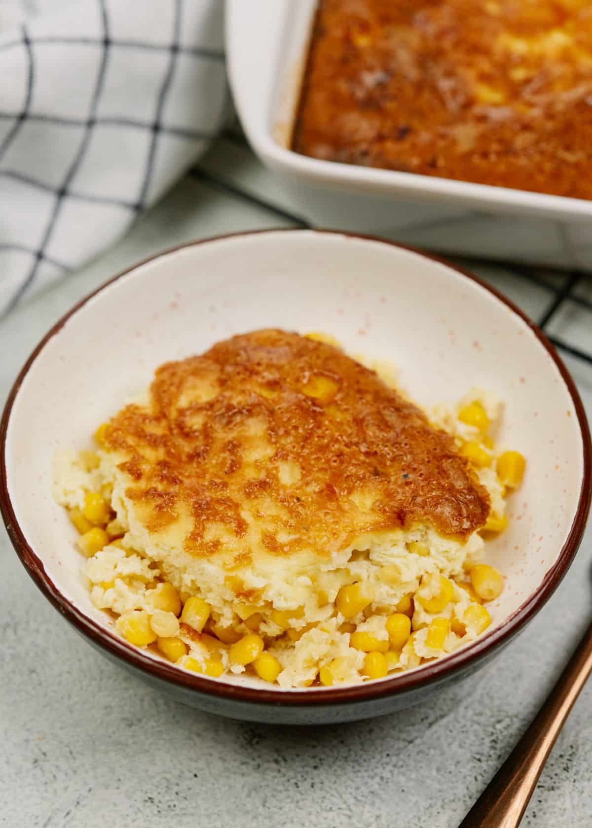 bowl of corn pudding casserole on table by striped white napkin