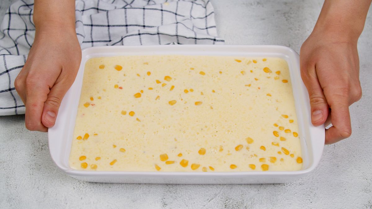 woman holding white baking dish filled with corn pudding before baking