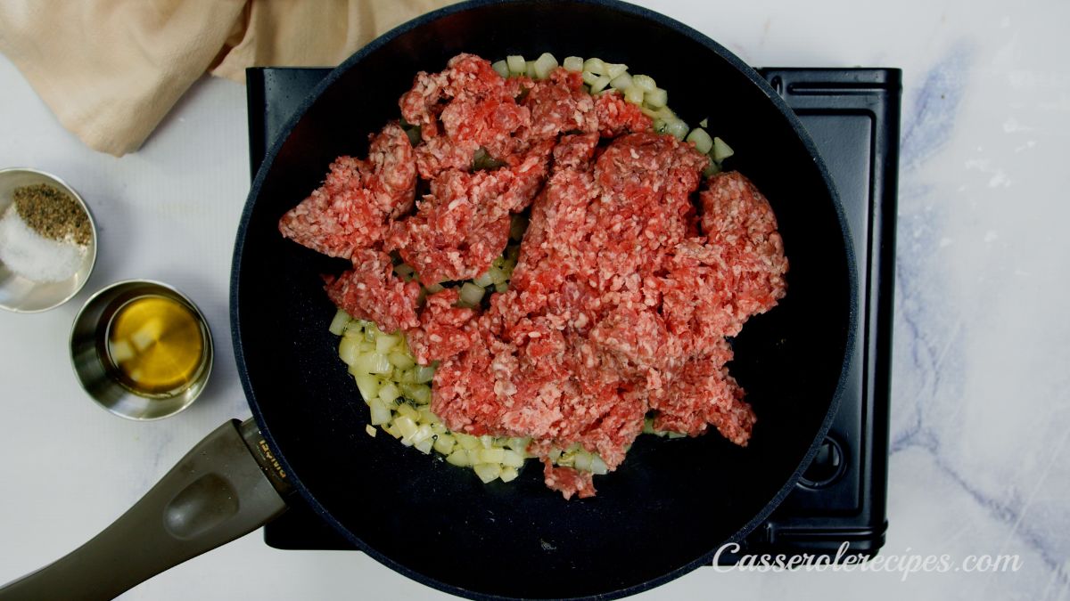 raw ground beef on top of onions in black skillet