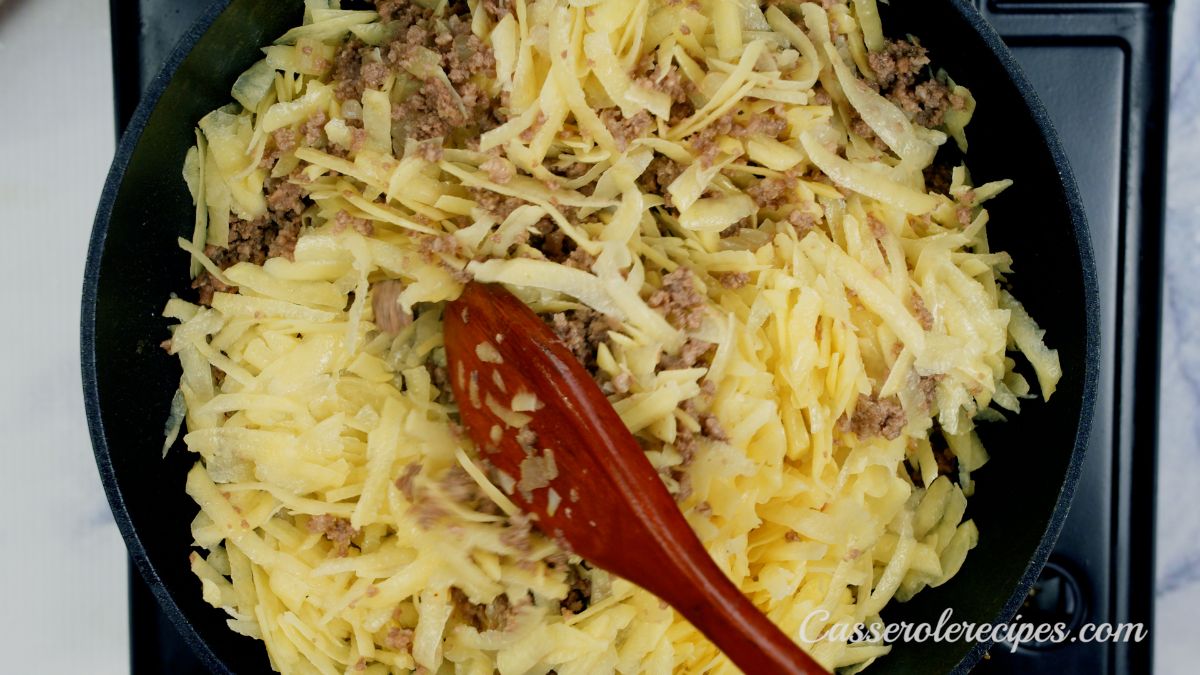 wooden spoon stirring beef and hashbrowns together to make gluten-free breakfast casserole
