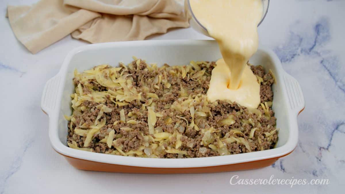 egg mixture being poured over hashbrowns and beef in baking dish