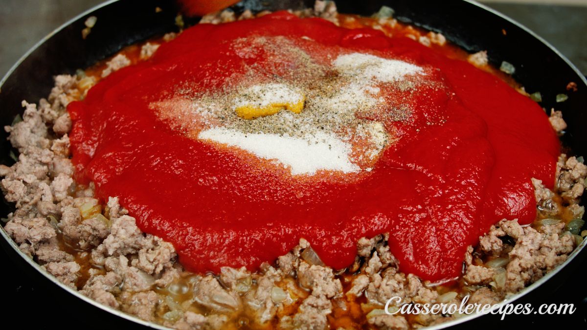 spices on top of red sauce in skillet of ground meat