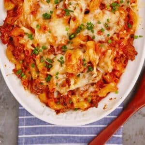 white baking dish of pasta and meat sauce topped with cheese and fresh herbs