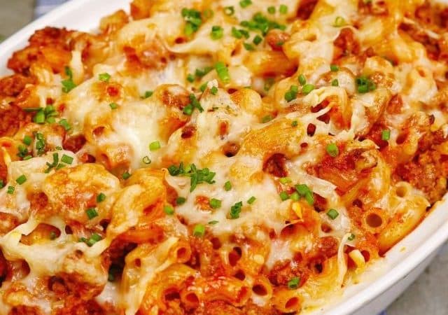 white baking dish of pasta and meat sauce topped with cheese and fresh herbs