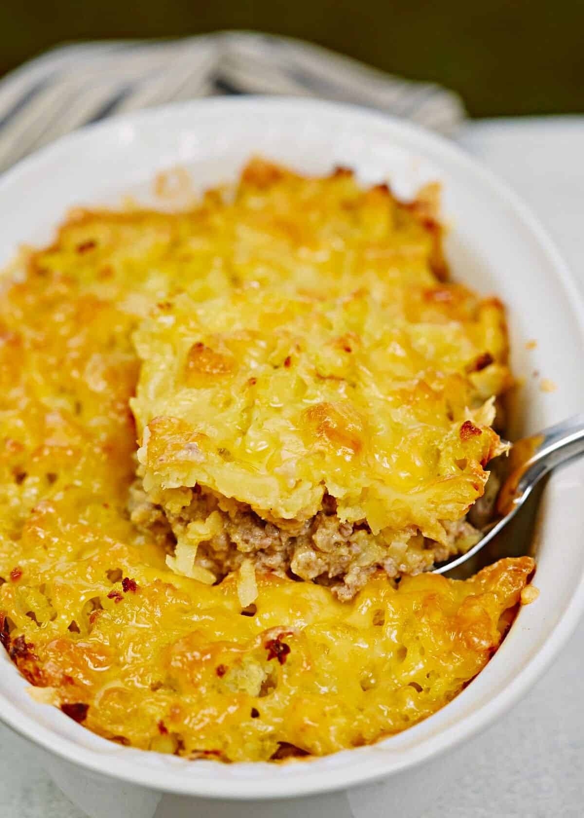 spoon in the side of white baking dish of hamburger potato casserole on white table