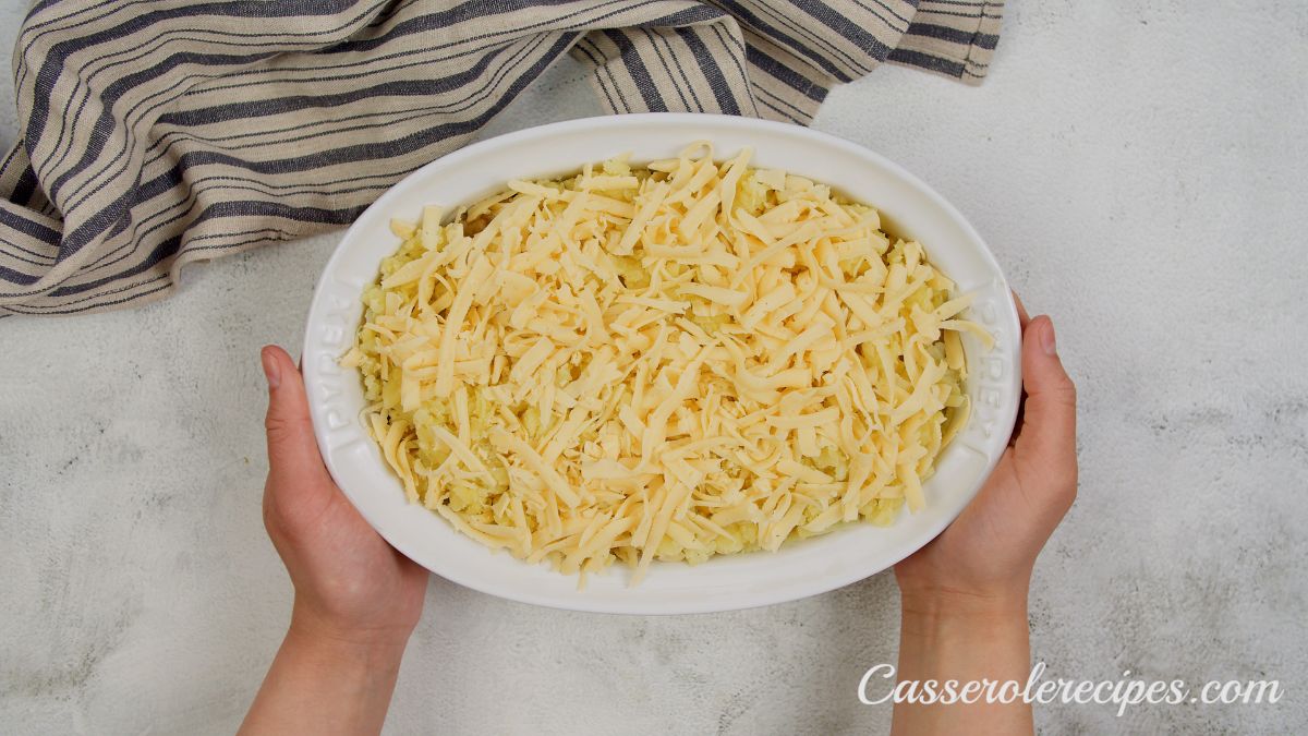 hands holding white casserole dish with cheese on top before baking