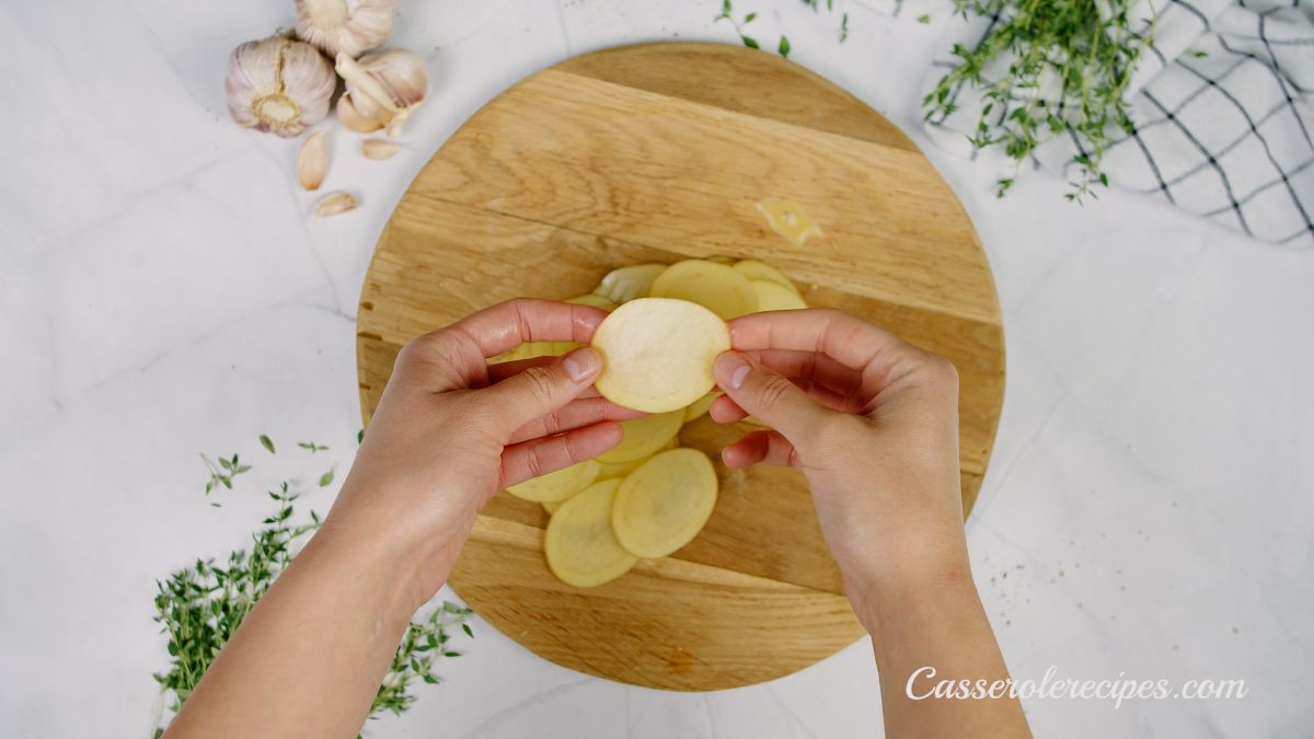 hand holding sliced potato above cutting board