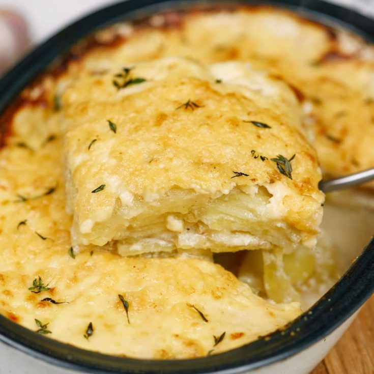 spoon of au gratin potatoes held above black and white baking dish