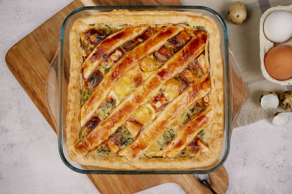 square glass baking dish of puff pastry breakfast casserole on top of wood cutting board