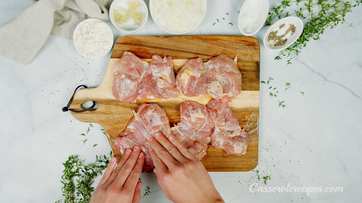 hands seasoning chicken thighs on cutting board