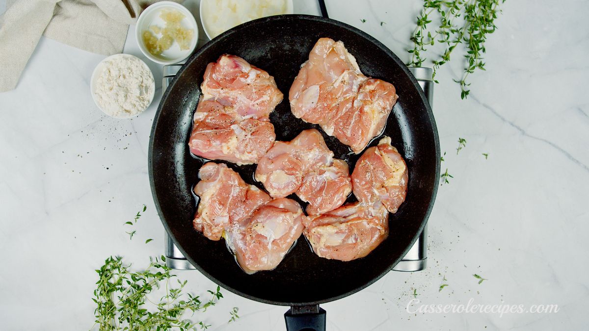 raw chicken thighs in black skillet on silver hot plate