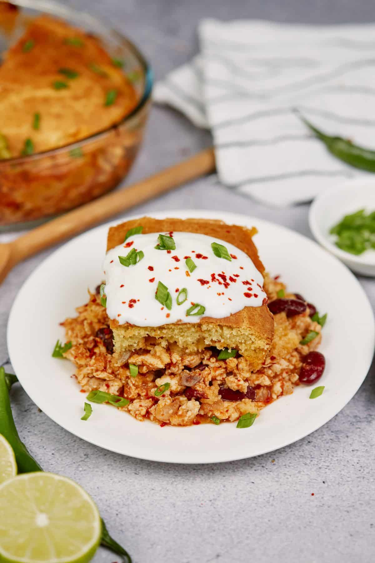 chicken tamale pie slice on white plate topped with sour cream
