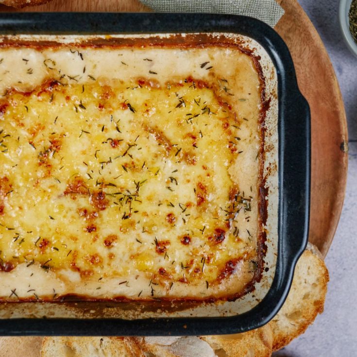 creamed onion gratin in square black baking dish with crusty bread