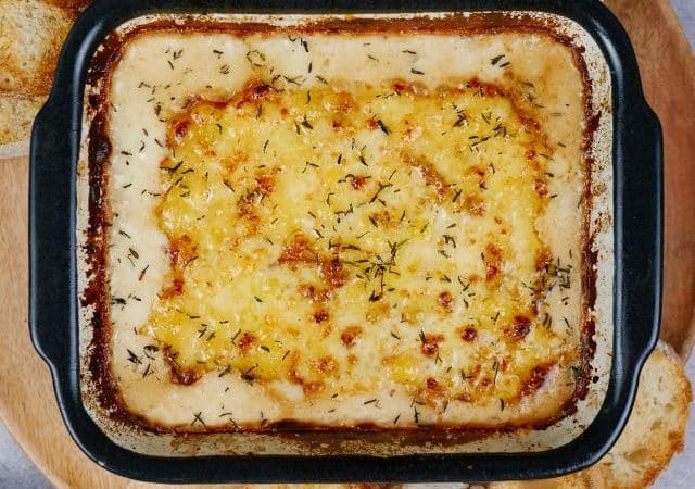 creamed onion gratin in square black baking dish with crusty bread