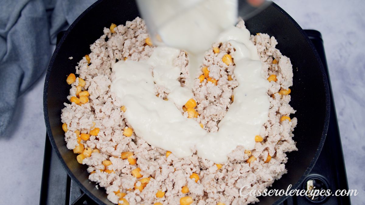 bechamel sauce being poured into skillet with ground turkey and corn