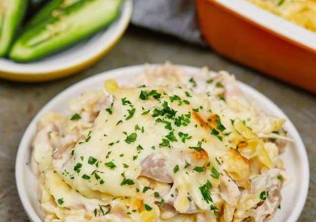 white plate of jalapeno popper chicken casserole on wood table by plate of jalapenos