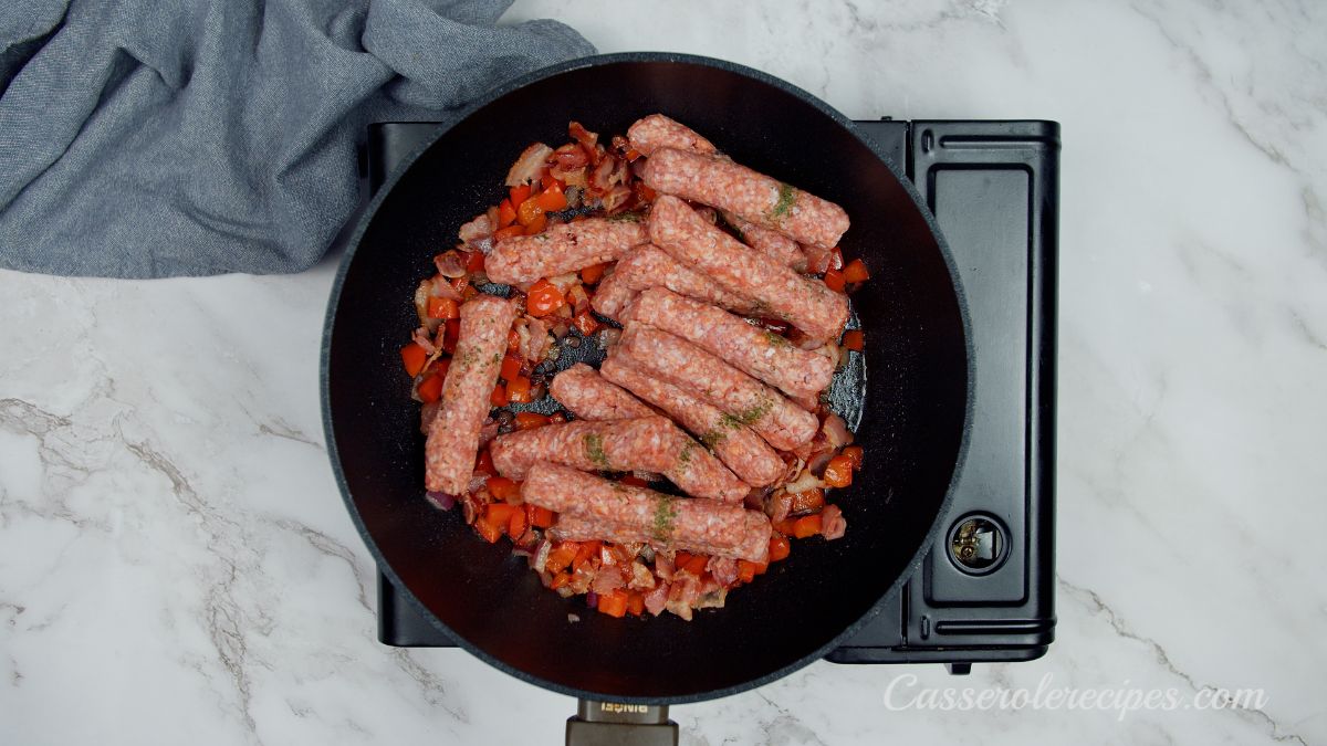 raw sausage links in skillet with red peppers