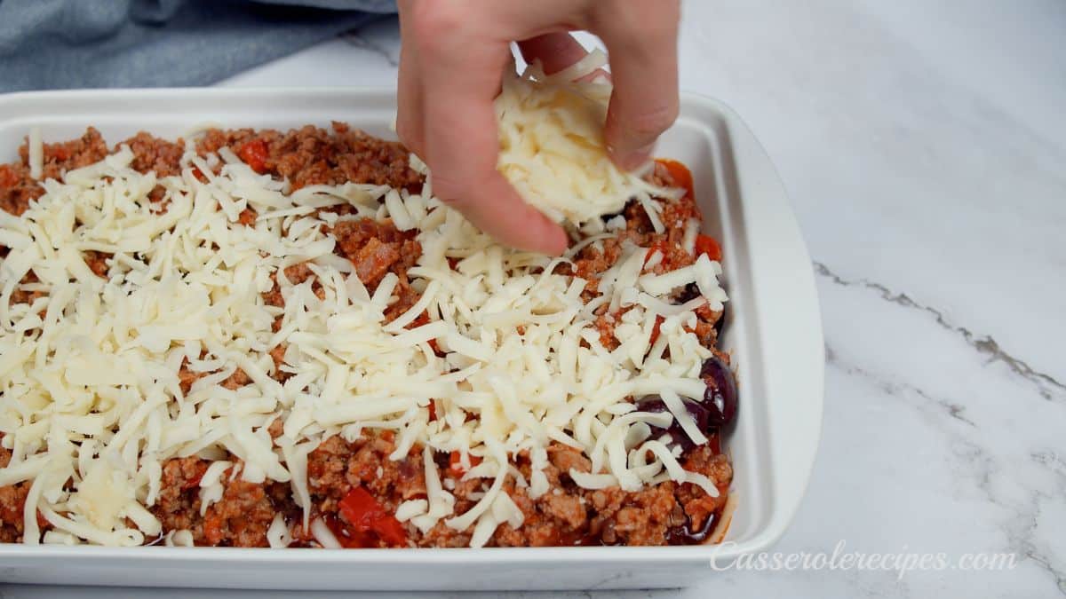 hand sprinkling cheese over pizza casserole