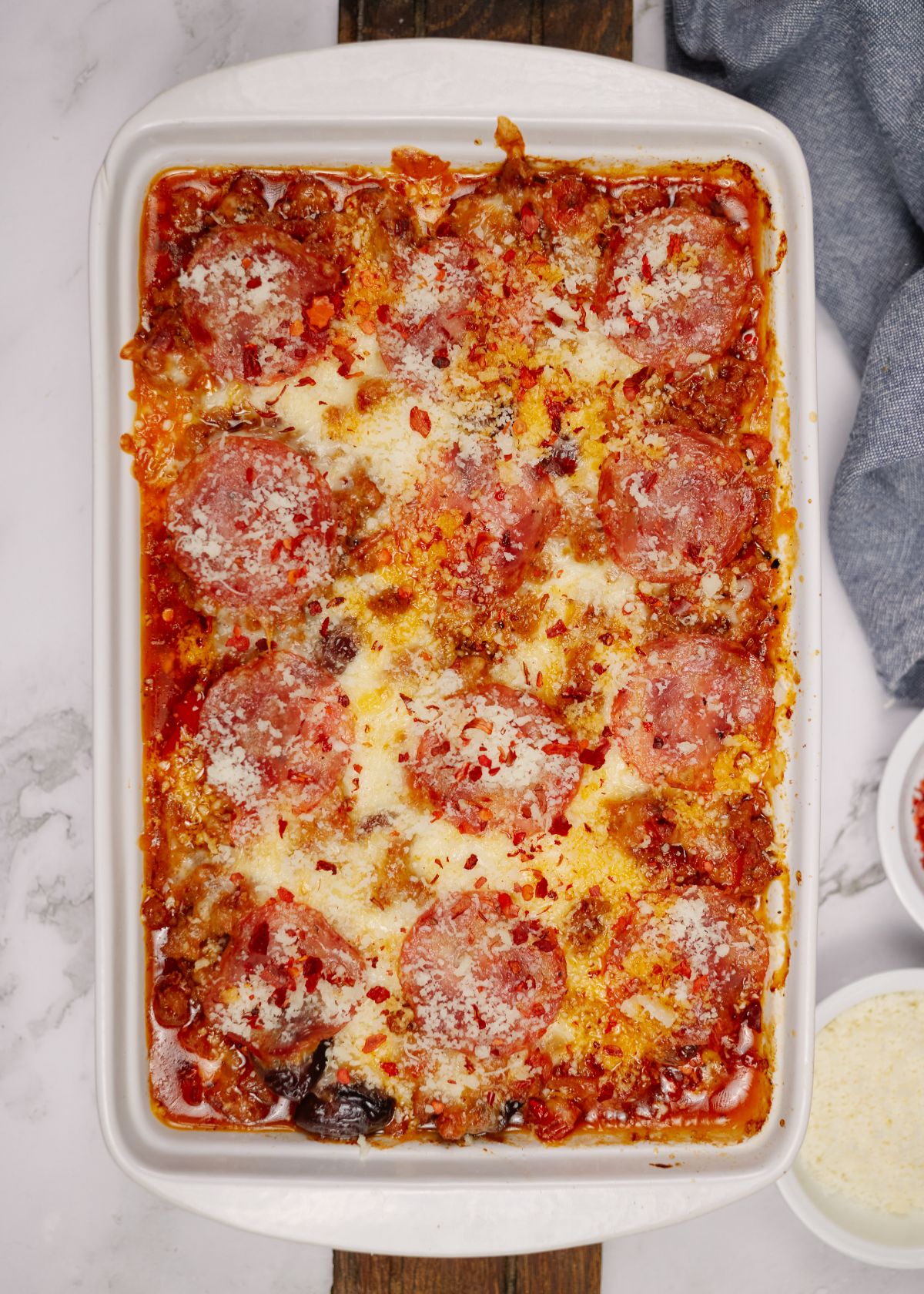 low carb pizza casserole in large white baking dish sitting on white table with blue cloth napkin