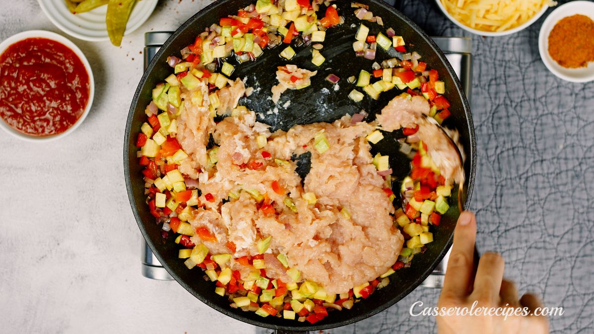 black skillet of peppers and onions with raw chicken being cooked