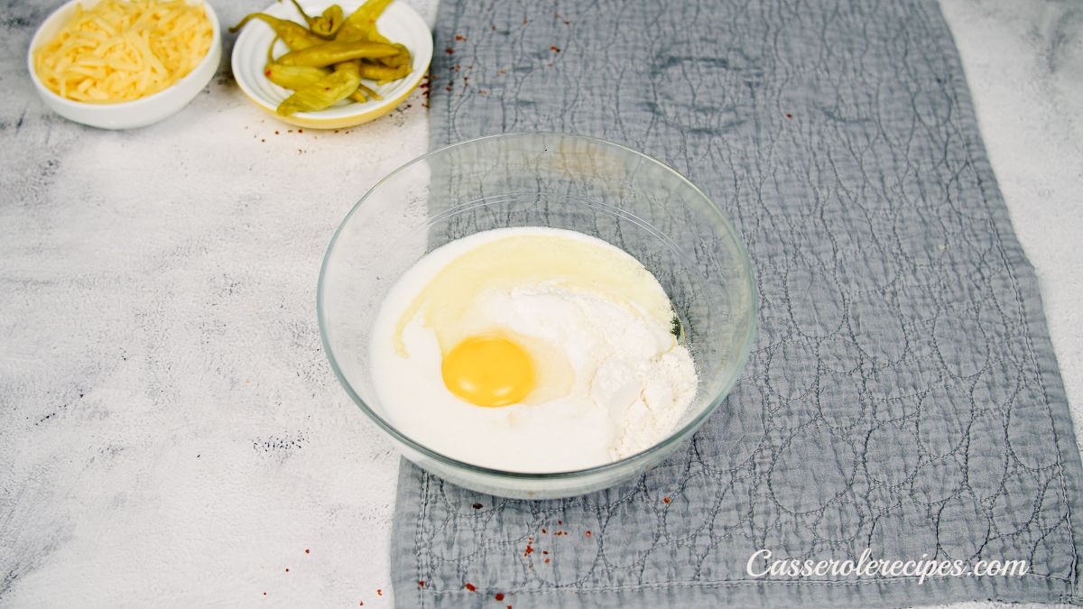 eggs and flour in glass bowl on counter with gray tablecloth