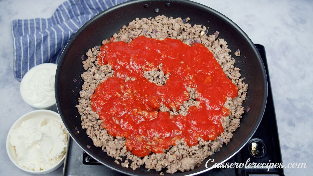 tomato sauce on top of ground beef in black skillet on hot plate