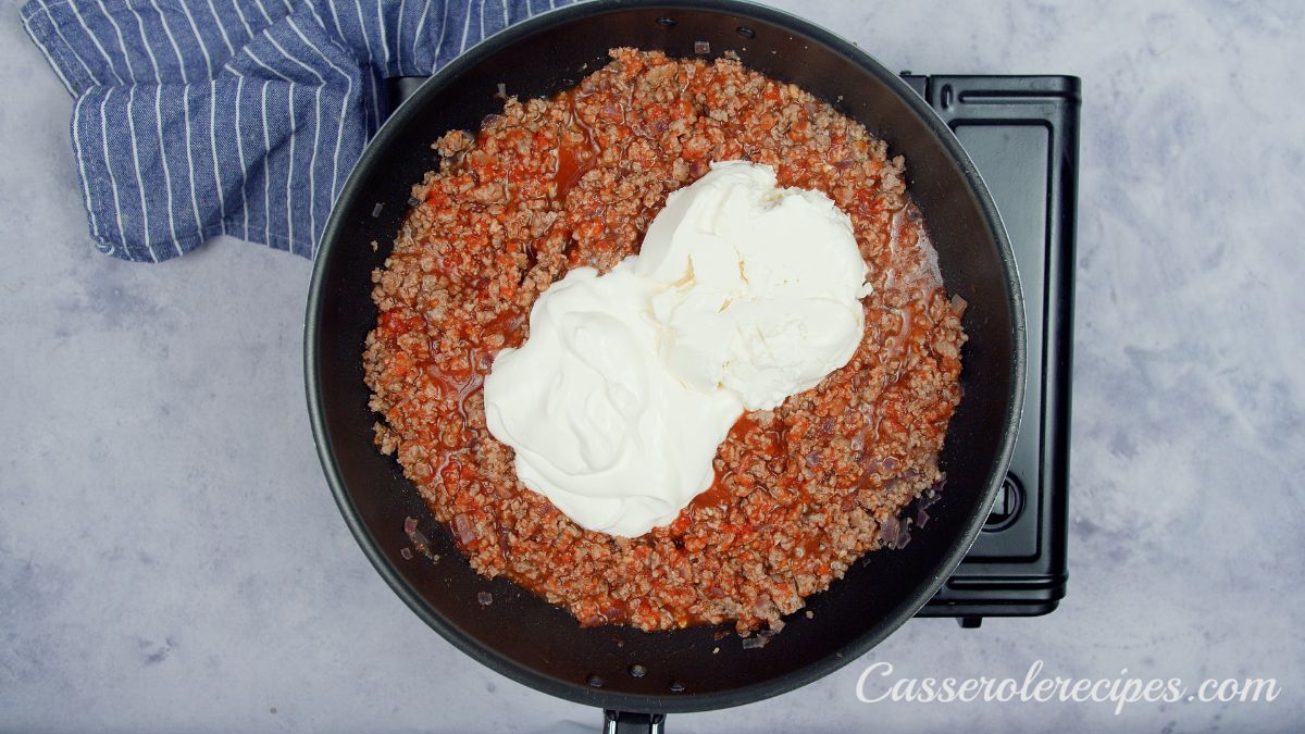 cheese on top of cooked ground beef and tomato sauce in skillet on hot plate