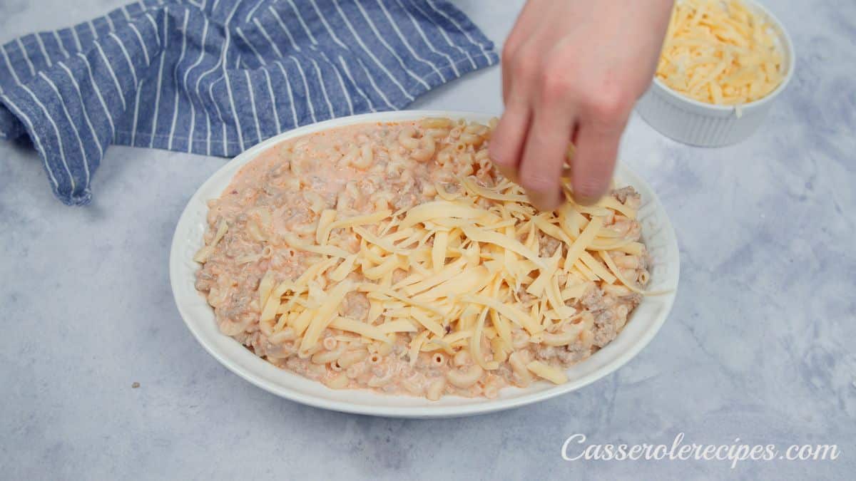 hand sprinkling cheese over top of hamburger casserole before baking